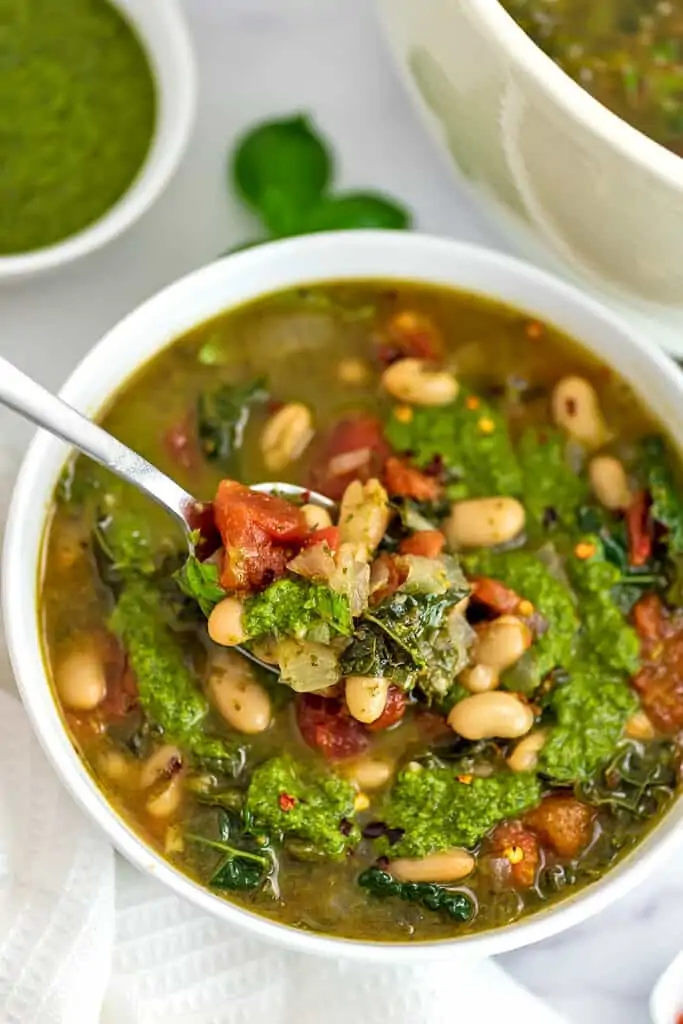 Spoon in bowl if Tuscan white bean soup with kale with pesto drizzled over top.