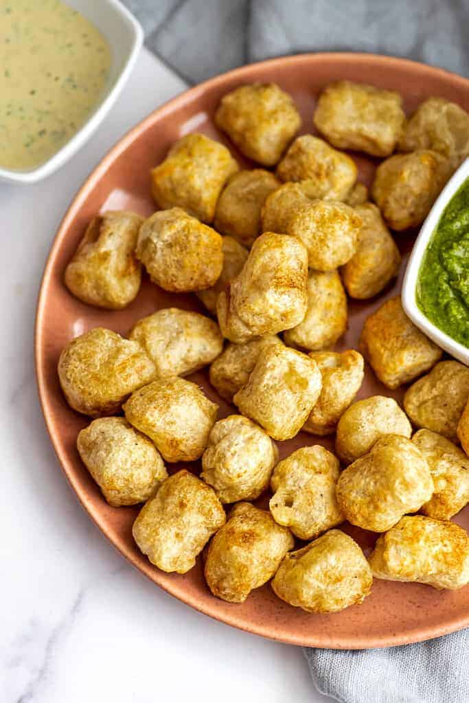 Air fryer cauliflower gnocchi on a pink plate with ramekin of pesto.