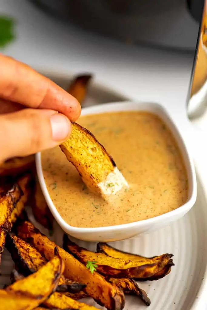 Hand dipping rutabaga fry in spicy sauce.