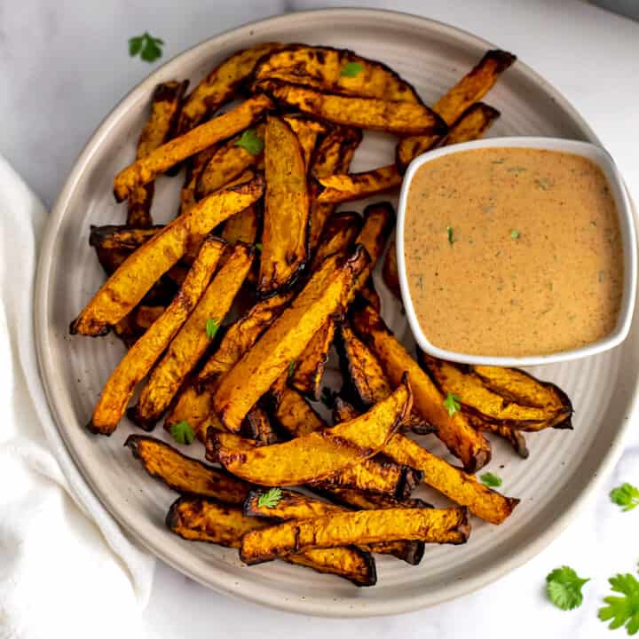 Rutabaga fries on a ivory plate with ramekin of spicy dipping sauce.