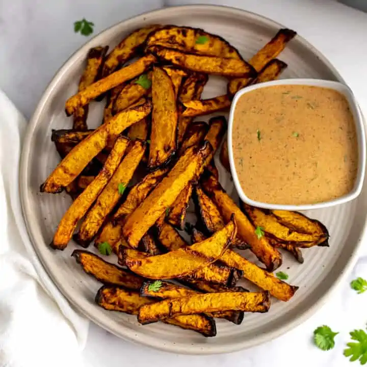 Rutabaga fries on a ivory plate with ramekin of spicy dipping sauce.
