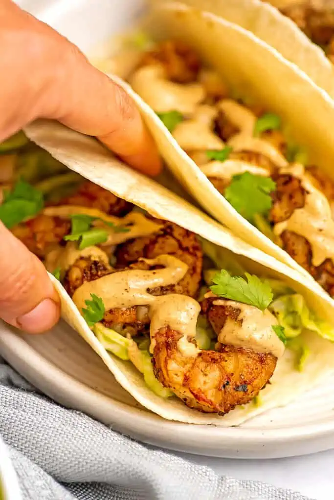 Air fryer shrimp tacos being held by a hand on white plate.