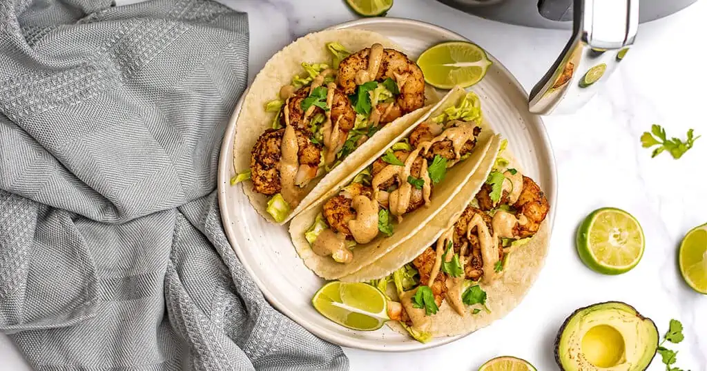 Three shrimp tacos on a white plate with a blue napkin.