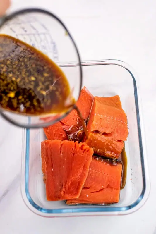 Teriyaki marinade being poured over salmon.