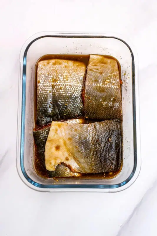 Salmon marinating in teriyaki sauce in a glass container.
