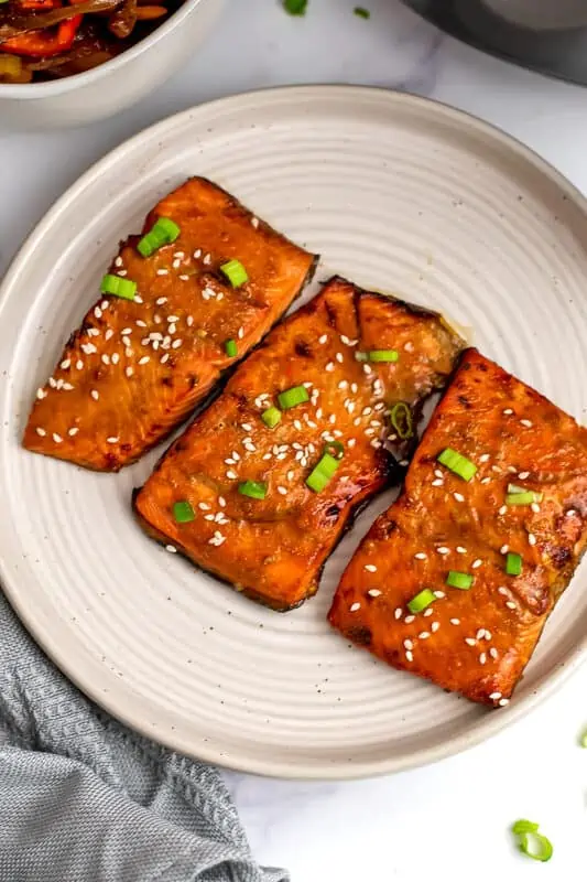 Air fryer teriyaki salmon on a white plate, blue napkin on the side.