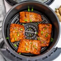 Salmon teriyaki in air fryer basket with green onions and sesame seeds on top.