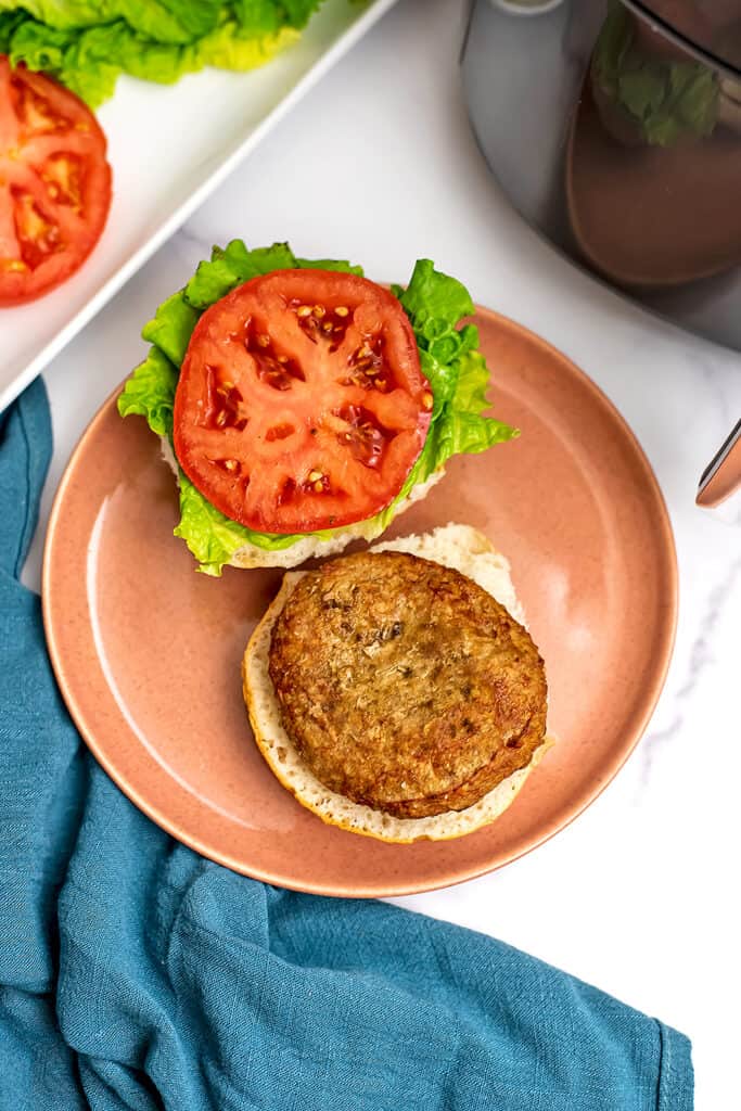 Air fryer frozen turkey burger on pink plate with lettuce and tomato on bun.