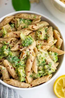 Creamy vegan broccoli pasta in a white bowl, lemons on the side.
