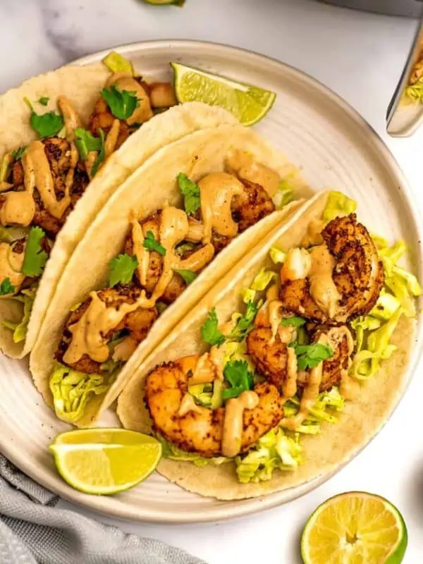 Three air fryer shrimp tacos on a white plate with limes.