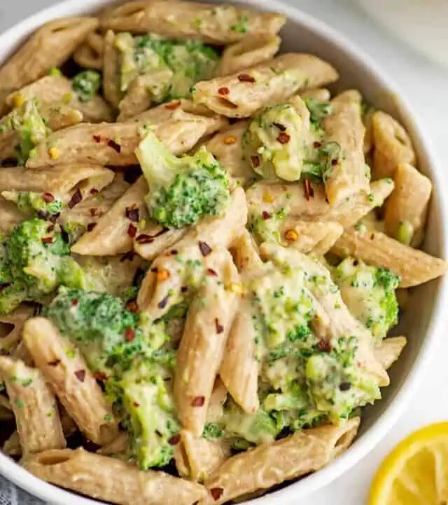 Creamy vegan broccoli pasta in a white bowl, lemons on the side.