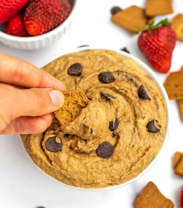 Hand dipping a cookie in a bowl filled with cookie dough hummus.