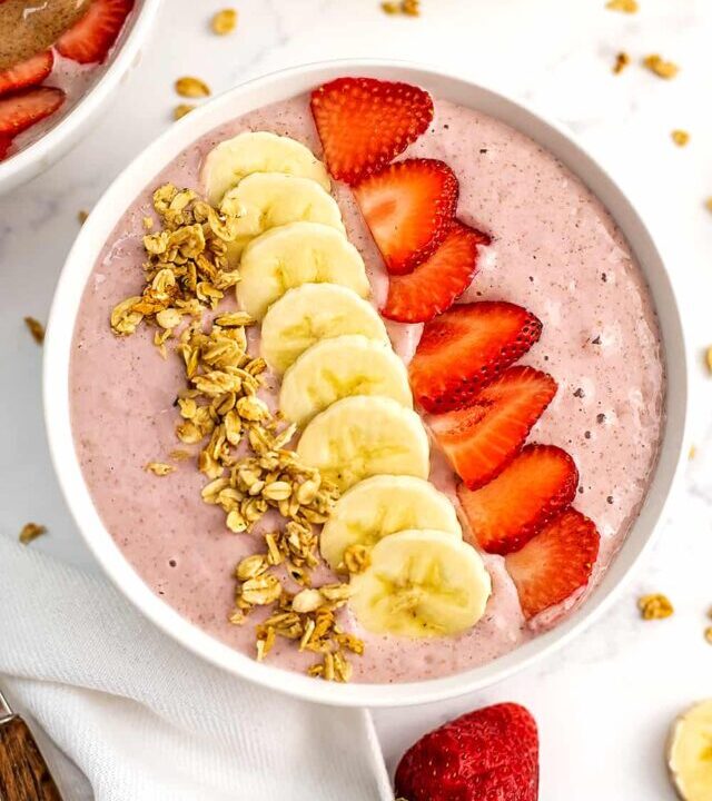 Sliced berries and bananas with granola on top of a banana strawberry smoothie bowl.