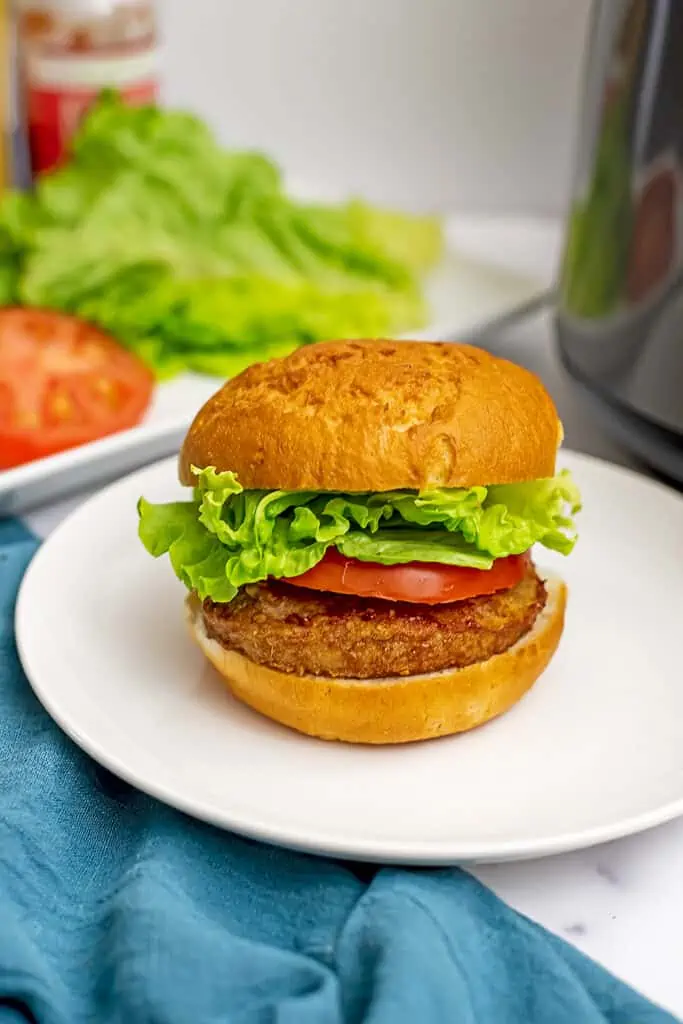 Air fryer frozen turkey burger on plate with lettuce and tomato on plate.