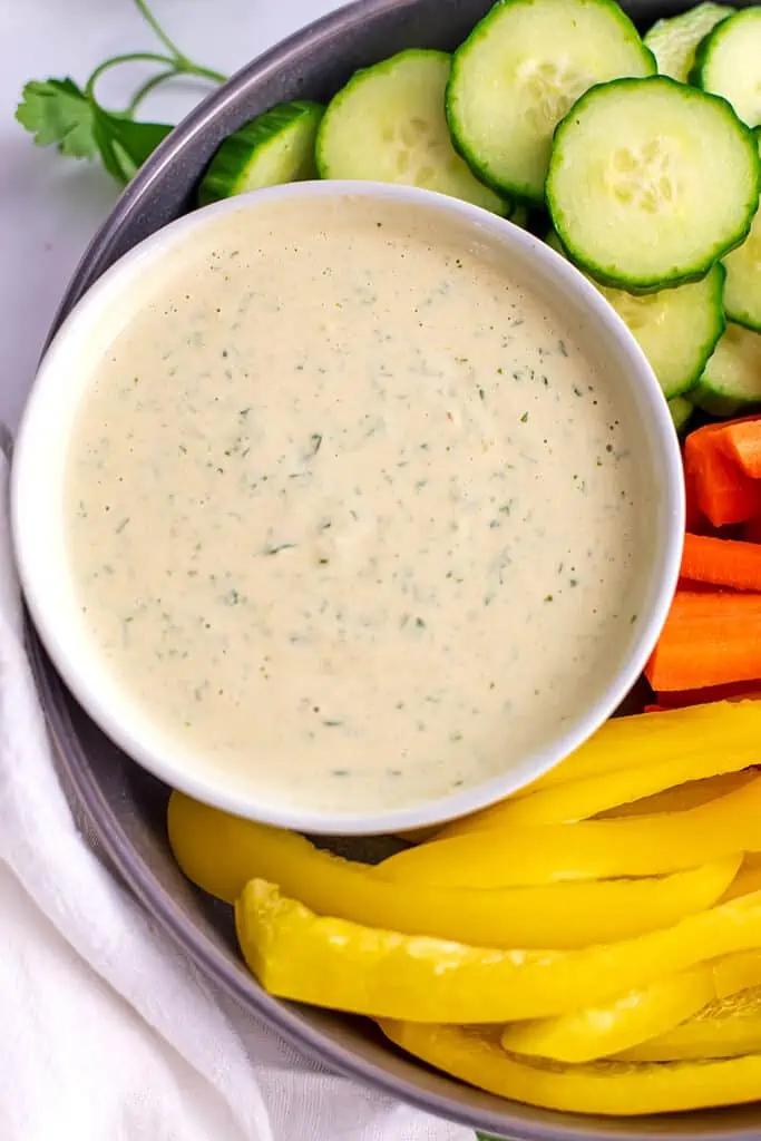 Lemon herb tahini sauce in a white bowl with sliced veggies in a platter.