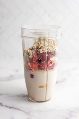 Ingredients to make strawberry banana smoothie bowl in a blender cup.