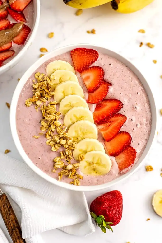 Sliced berries and bananas with granola on top of a banana strawberry smoothie bowl.
