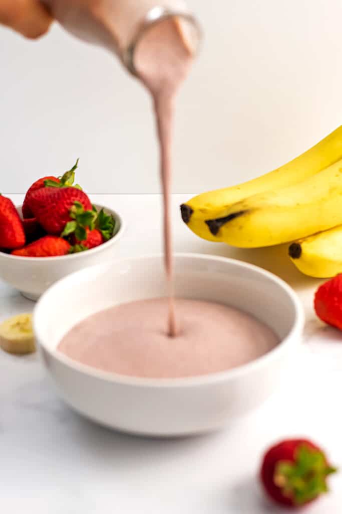 Strawberry banana smoothie being poured into a bowl.