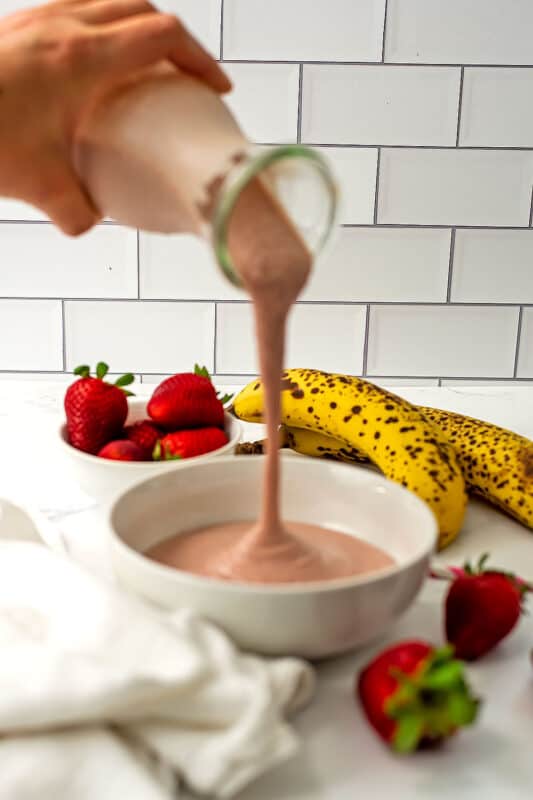 Strawberry banana smoothie being poured into a bowl.
