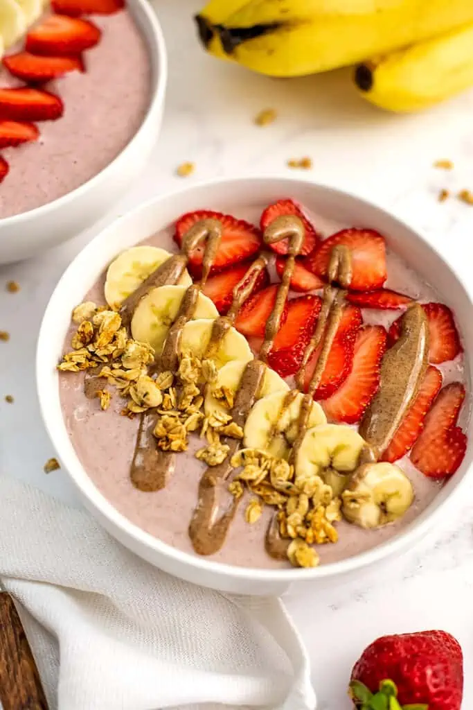 Banana strawberry smoothie bowl in a bowl with strawberries, bananas and granola with almond butter.