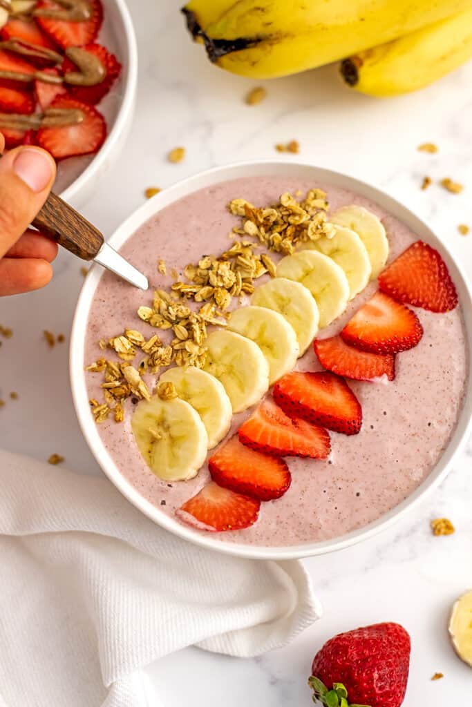 Wooden spoon rested in a strawberry banana smoothie bowl.