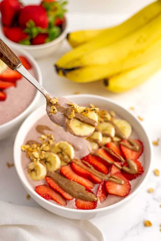 Strawberry banana smoothie bowl with sliced bananas and strawberries, with spoon of smoothie.