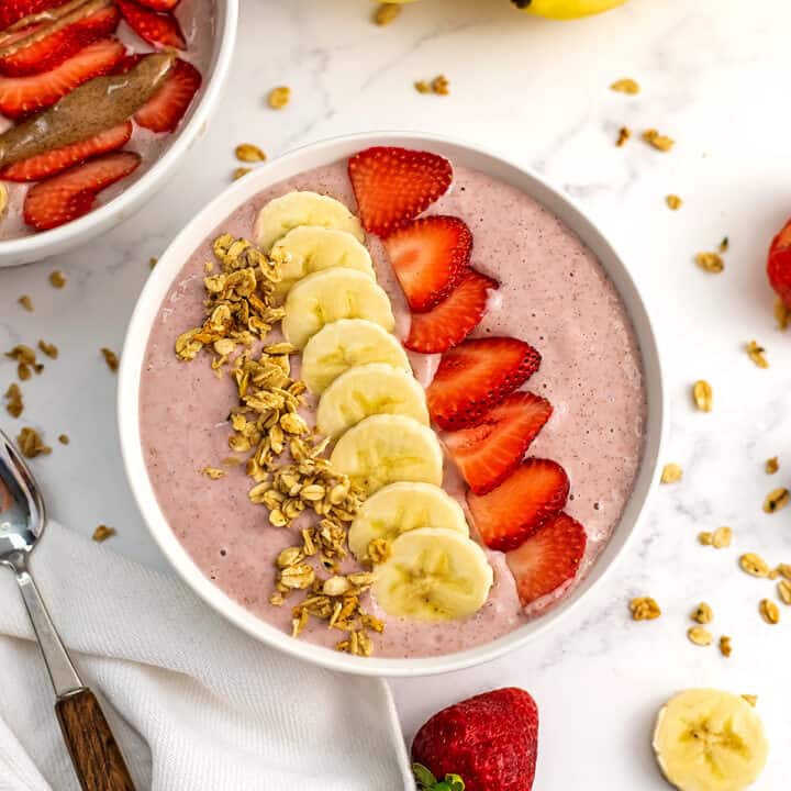 Strawberry banana smoothie bowl in white bowl with bananas, strawberries, granola on top.