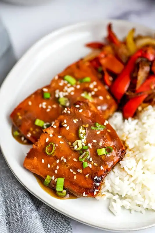 Air fryer teriyaki salmon next to rice and veggies on a white plate.