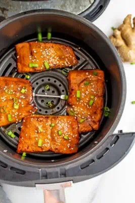 Salmon teriyaki in the air fryer basket, fresh ginger on the side.
