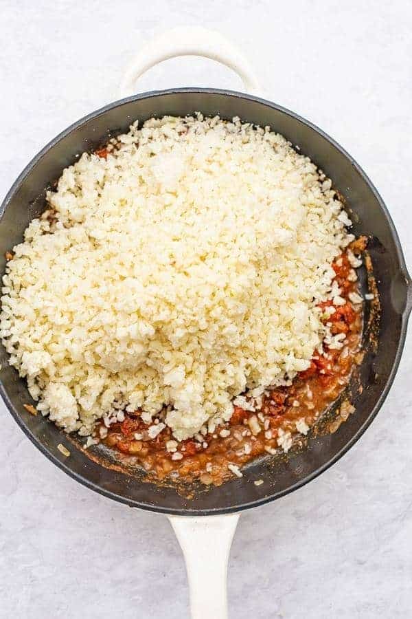 Frozen cauliflower rice added to skillet with tomato mixture.