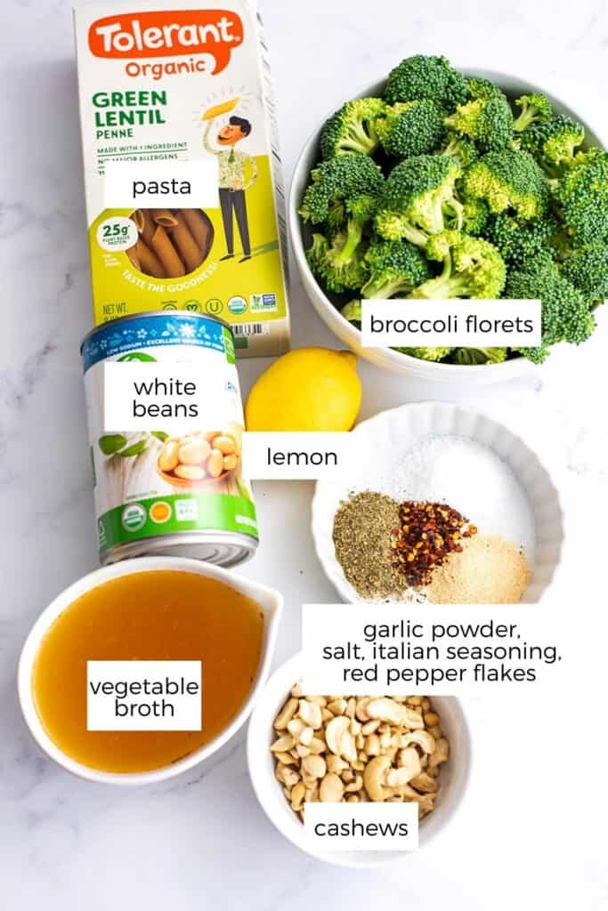 Ingredients to make vegan broccoli pasta in ramekins on a marble countertop.