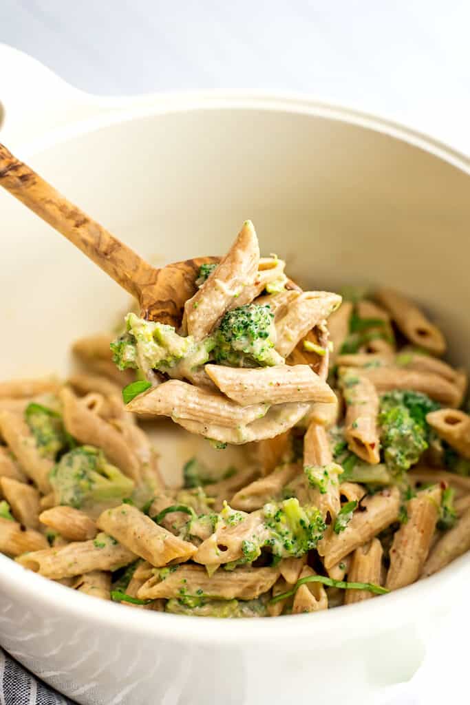 Wooden spoon with a serving of vegan broccoli pasta over a white pot.