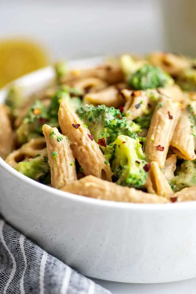 White bowl with creamy vegan broccoli pasta, blue napkin on the side.