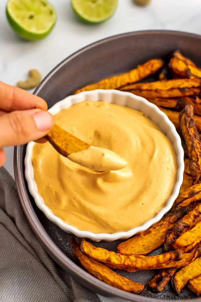 Hand dipping french fry in a ramekin filled with spicy vegan mayo.