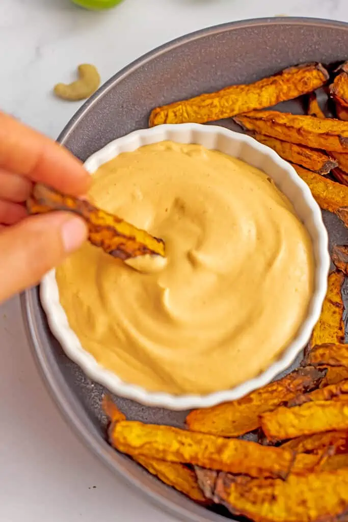 Hand dipping fries in vegan sriracha mayonnaise.