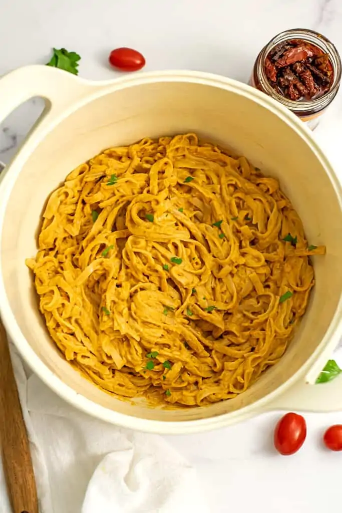 Creamy vegan sundried tomato alfredo pasta in a white pot.
