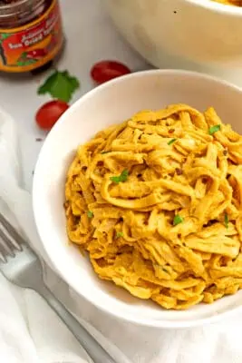 Vegan sun dried tomato alfredo pasta in a white bowl, fork on the side.