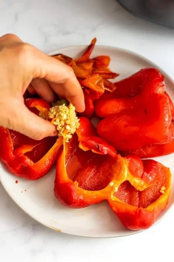 Hand removing the seeds and stem from roasted red peppers.
