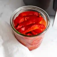 Roasted red peppers cut into slices in a glass jar.