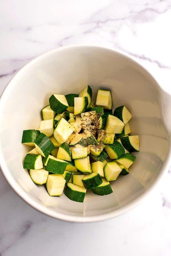 White bowl filled with cubed zucchini with spices on top.