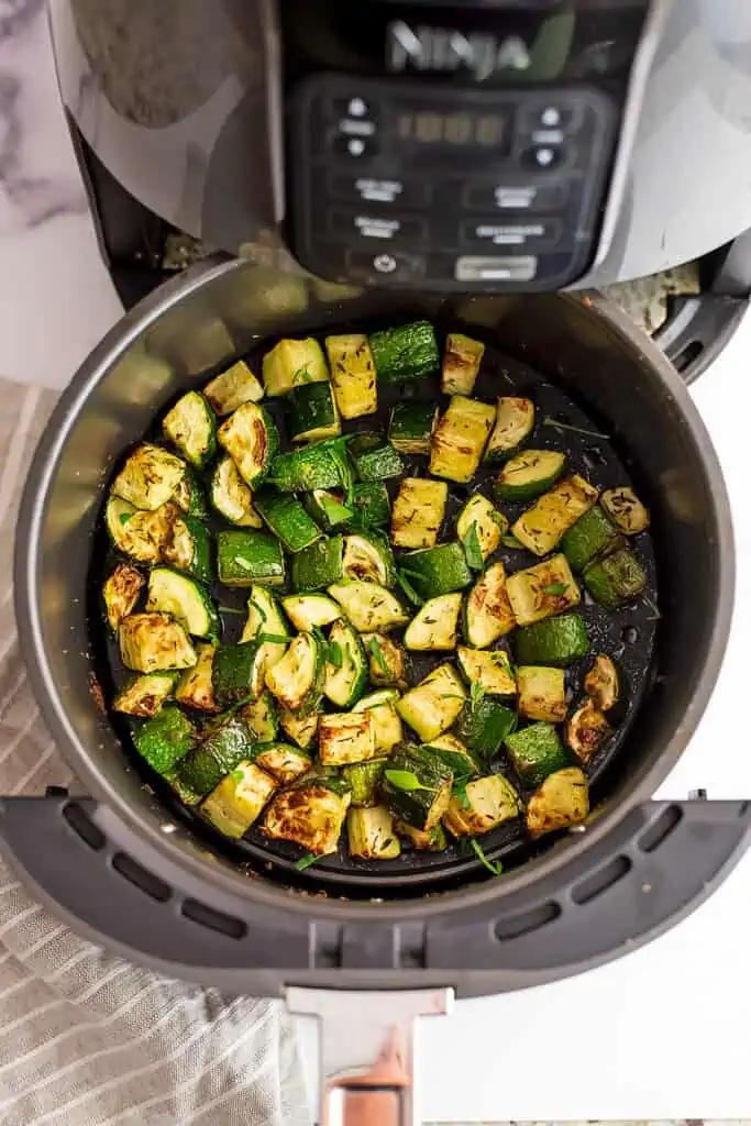 Roasted zucchini in an air fryer basket, beige striped napkin on the side.