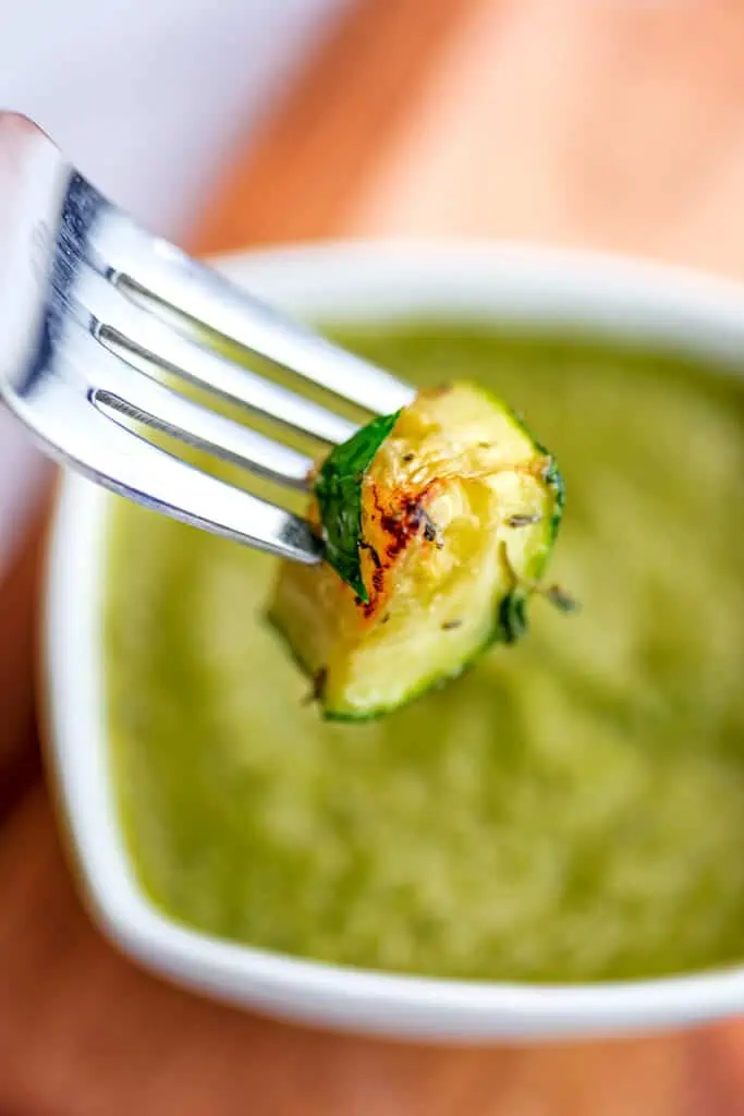 Fork with roasted zucchini being dipped in pesto..