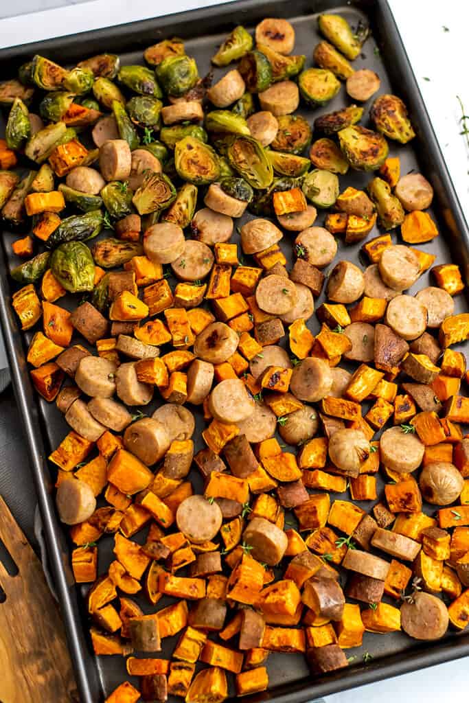 Sheet pan filled with chicken apple sausage, sweet potatoes and brussels sprouts.