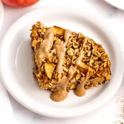 Slice of apple oatmeal bake on a white plate drizzled with almond butter.