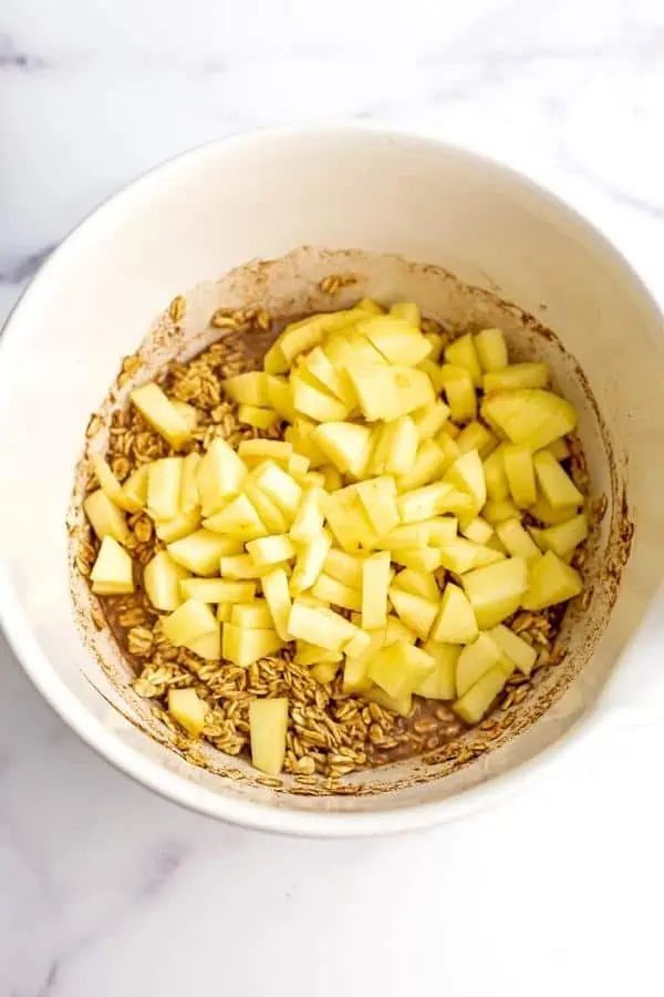 Chopped apples added to oatmeal mixture in white bowl.