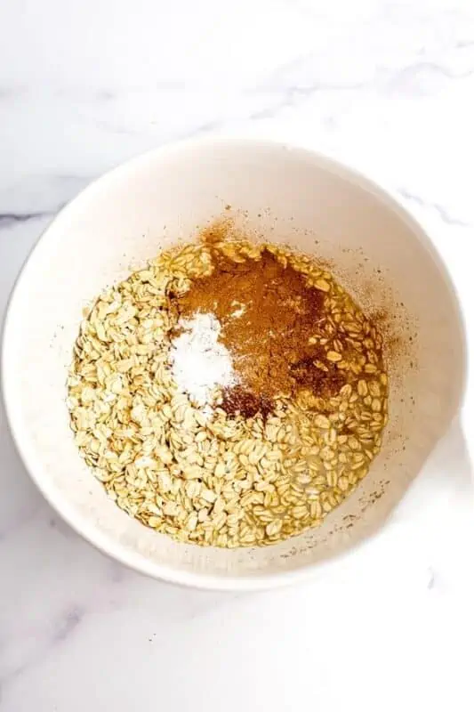 Oats, spices and baking powder added to a large white bowl.