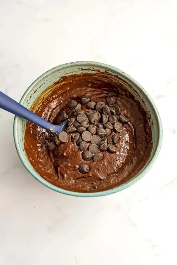 Chocolate chips added to brownie batter in blue bowl.
