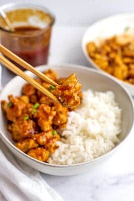 Wooden chopsticks picking up a sweet and sour cauliflower.