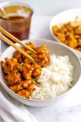 Wooden chopsticks picking up a sweet and sour cauliflower.
