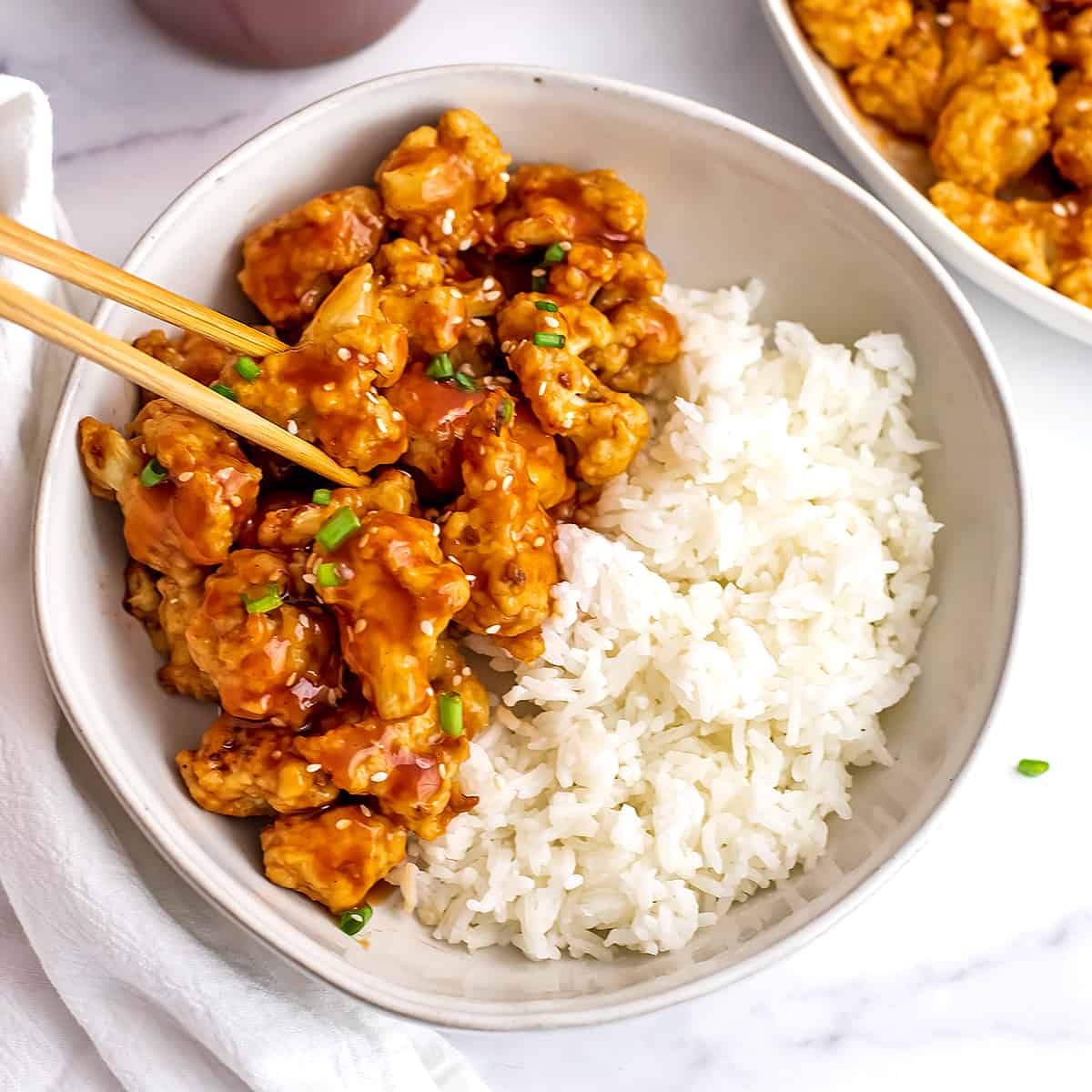 Chopsticks getting a serving of sweet and sour cauliflower from the plate with white rice.
